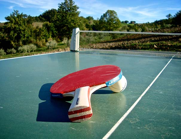 Inquadratura ravvicinata di una racchetta e una pallina utilizzate per giocare a ping pong adagiate su un tavolo da gioco.