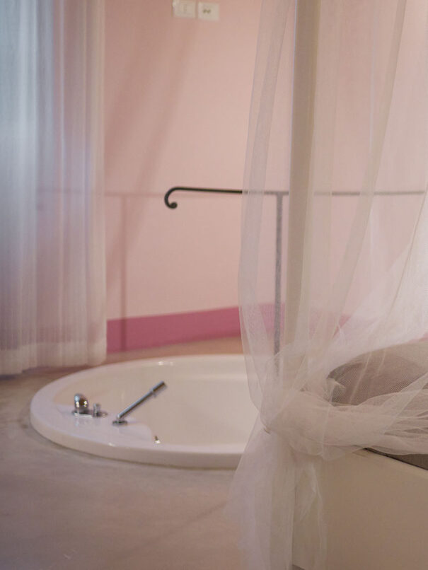 Al centro della foto, è posizionato un angolo del letto matrimoniale con tende che si trova all’interno della suite Le Lavande dell’Agriturismo Montelovesco. Ai piedi del letto, si trova una vasca da bagno a filo pavimento.