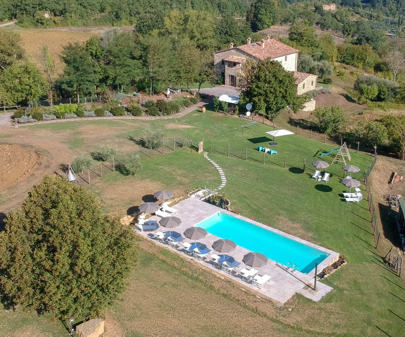 Foto panoramica dall’altro dell’intero complesso dell’Agriturismo Montelovesco. Circondato dalle colline umbre, al centro della foto, si trova la struttura e poco distante, spostandosi verso il basso della foto, si trova la piscina appartenente all’agriturismo. Il complesso è circondato da grandi giardini, terreni per le pratiche agricole e alberi di ogni genere.